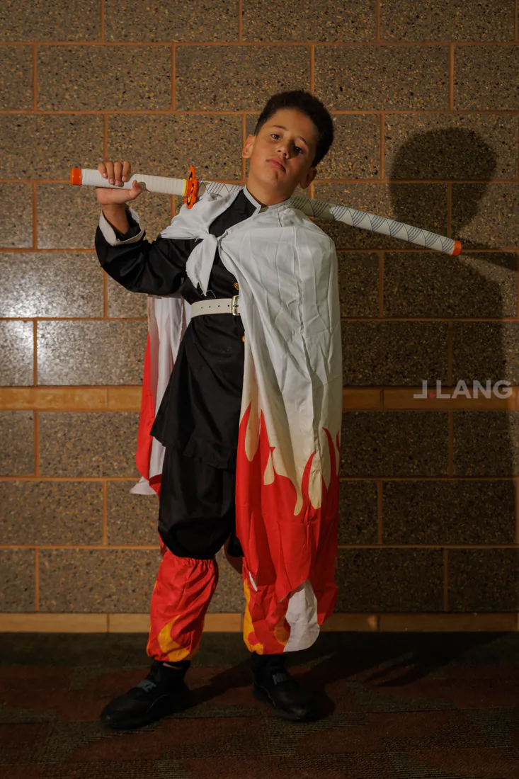 Boy in a flame-trimmed white cape rests a prop sword across his shoulders
