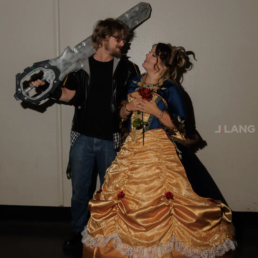 A man with a giant key-shaped sword smiles at a woman in a gold ball gown
