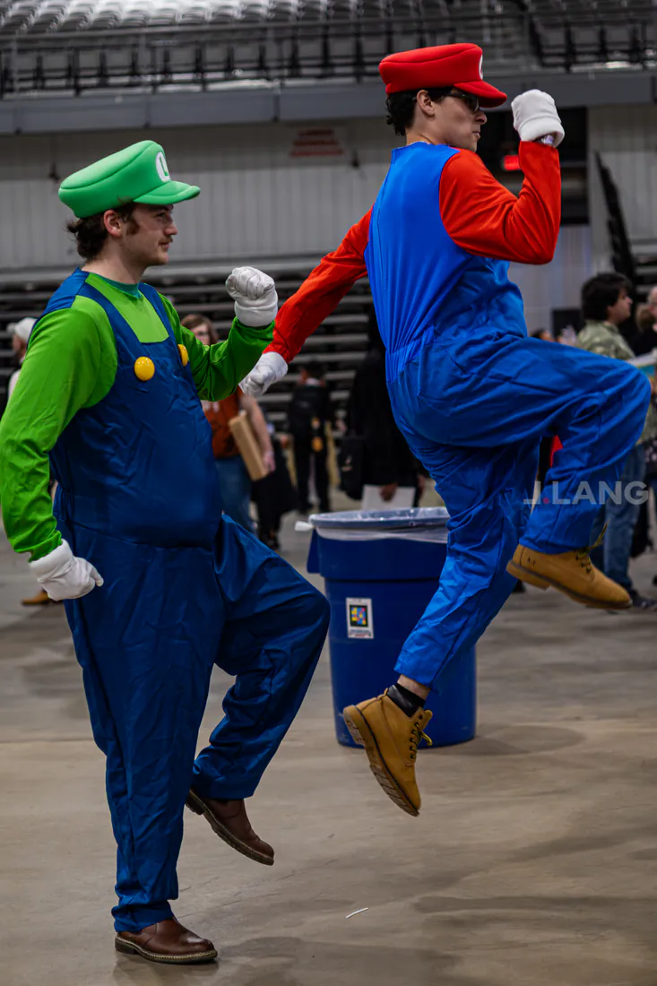 Cosplayers dressed as Mario and Luigi high-step across an arena floor, Mario in midair