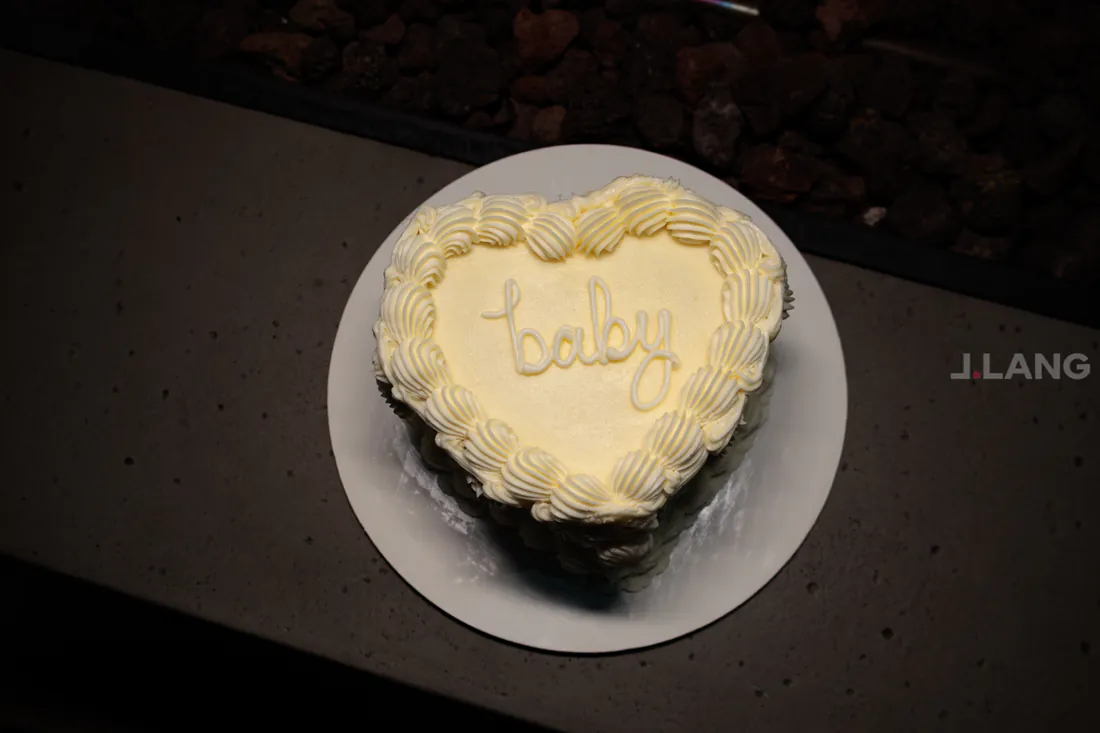 Heart-shaped cake with piped white frosting and the word baby written across the top