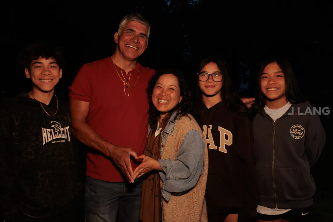 Family of five smiling at night, two adults joining hands in a heart shape