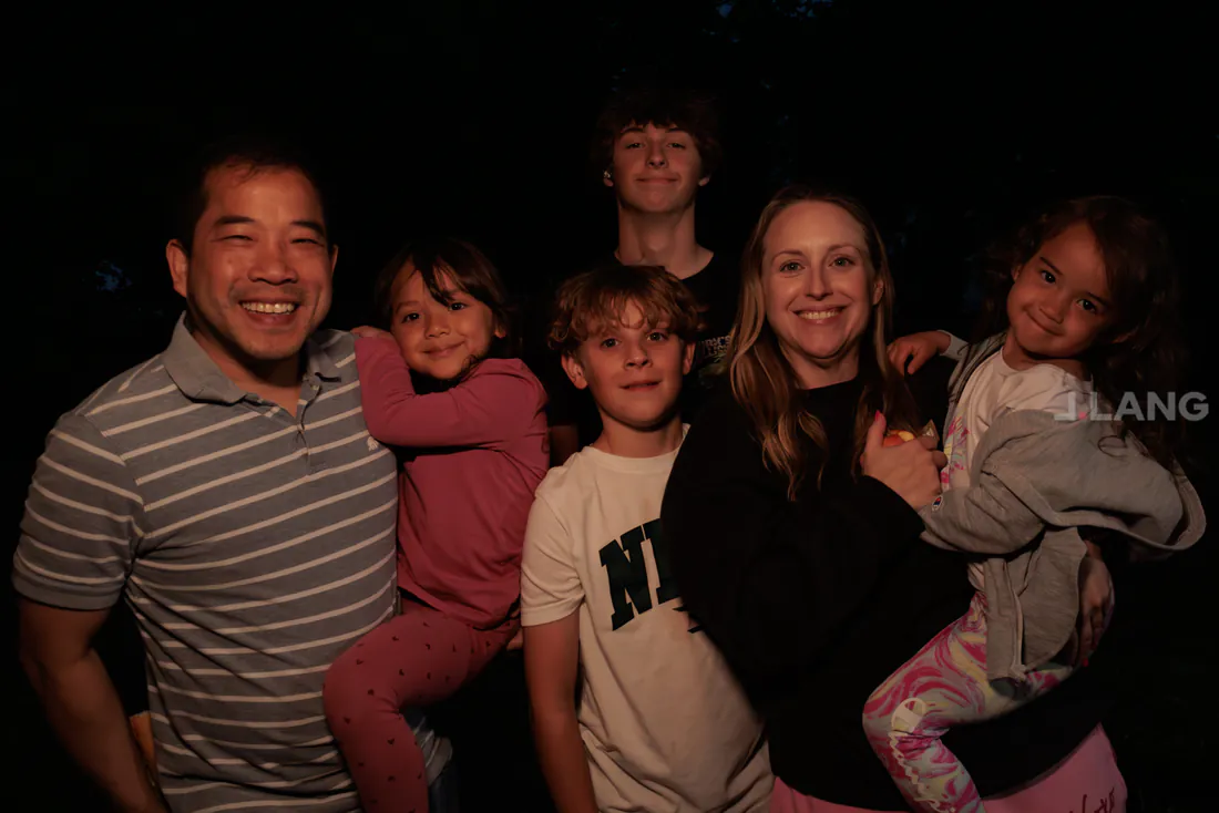 Family of six smiling close together at night, two little girls held in arms