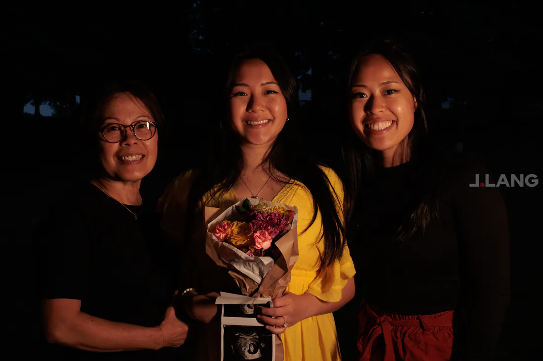 Three smiling women, the center one in yellow holding flowers and ultrasound prints