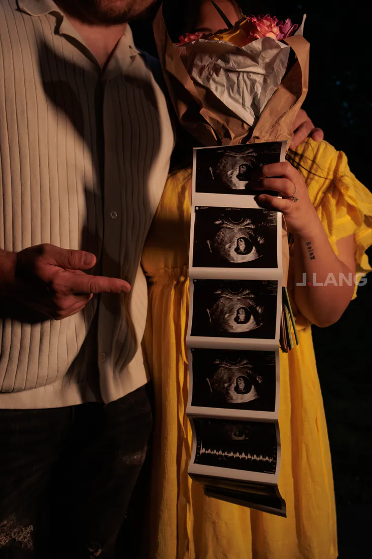A man points at a strip of ultrasound prints held by a woman in yellow