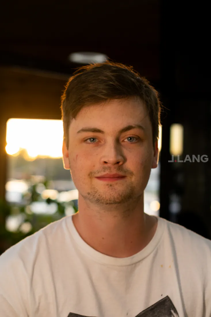 Young man in a white T-shirt with a soft smile, golden window light behind him