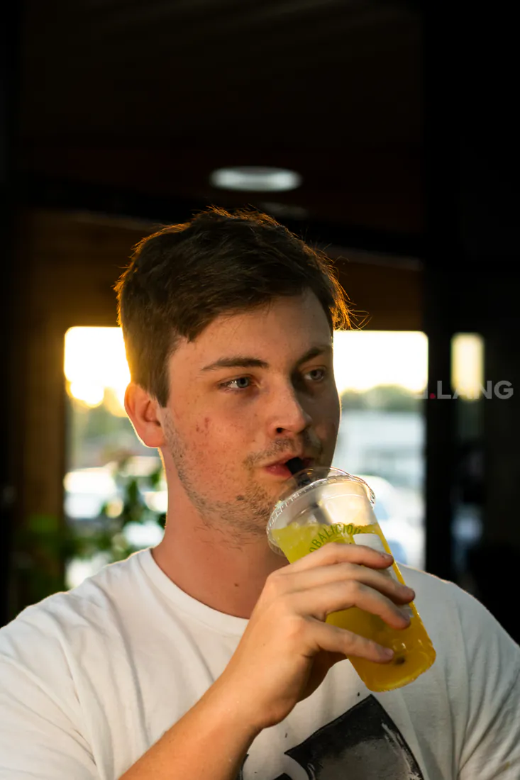Young man in a white T-shirt sips an iced yellow drink through a straw
