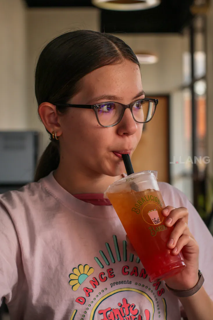 Girl in glasses and a graphic pink T-shirt sipping a red and amber iced tea