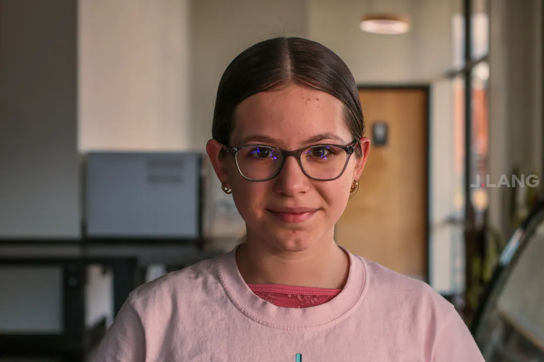 Girl with hair pulled back, glasses and a pink T-shirt giving a gentle closed-mouth smile
