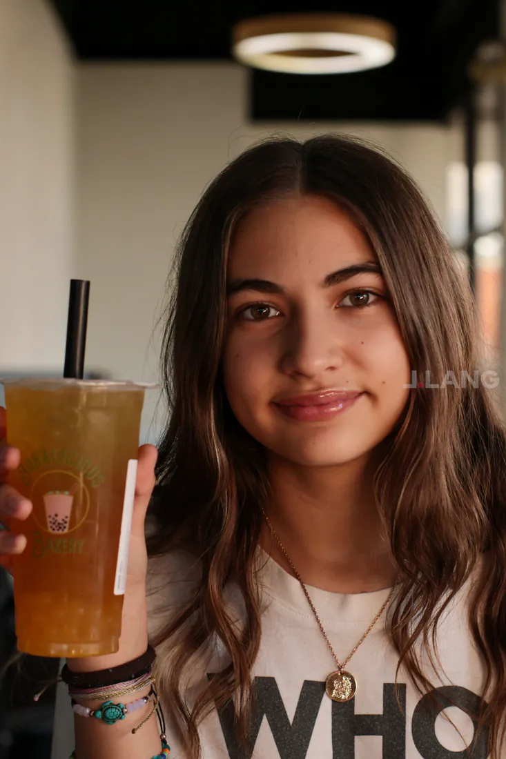 Long-haired teen girl smiles while holding up a golden iced tea beside her face