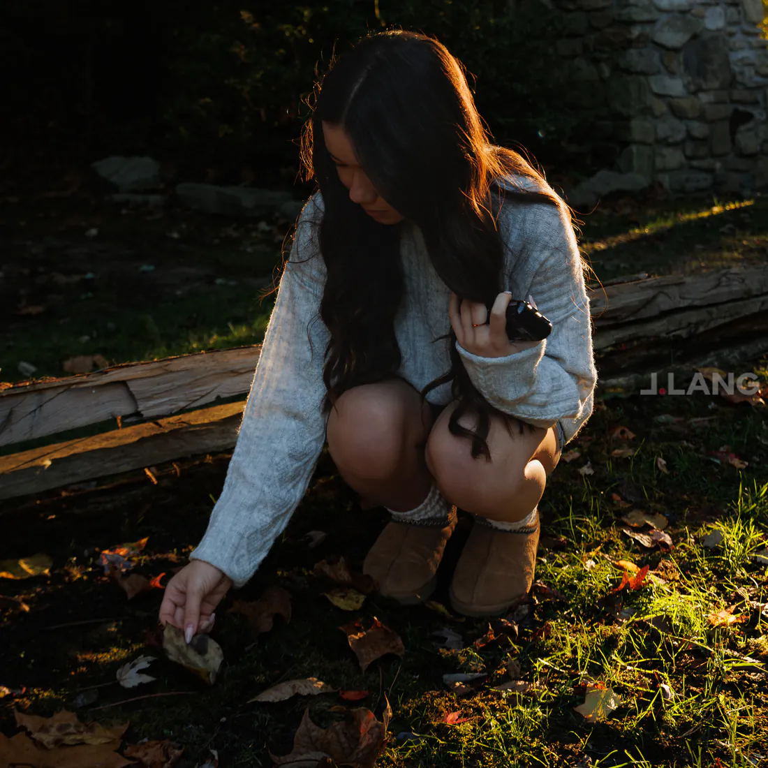Young woman crouches to touch a fallen leaf, long dark hair partly covering her face