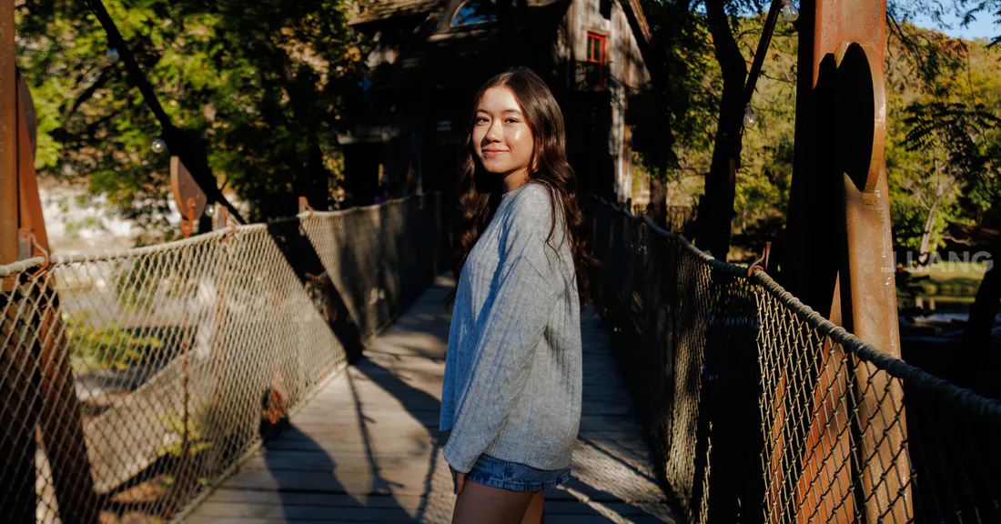 A young woman in a light knit sweater smiles over her shoulder on a suspension bridge