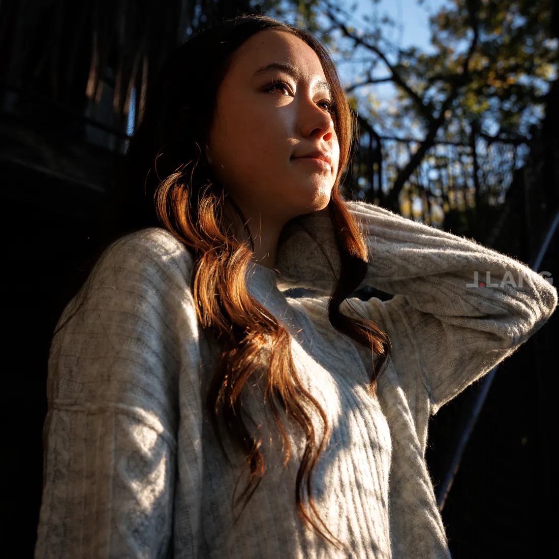 Young woman in a light gray sweater looks up and away in golden side light