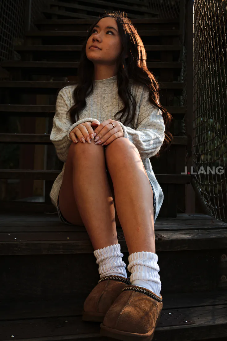 Young woman in a sweater and slouch socks sits on wooden stairs, gazing upward