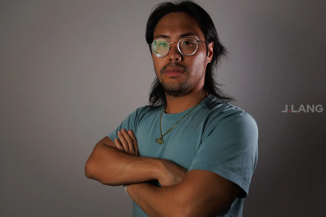 A serious man in round glasses and a teal T-shirt with his arms folded